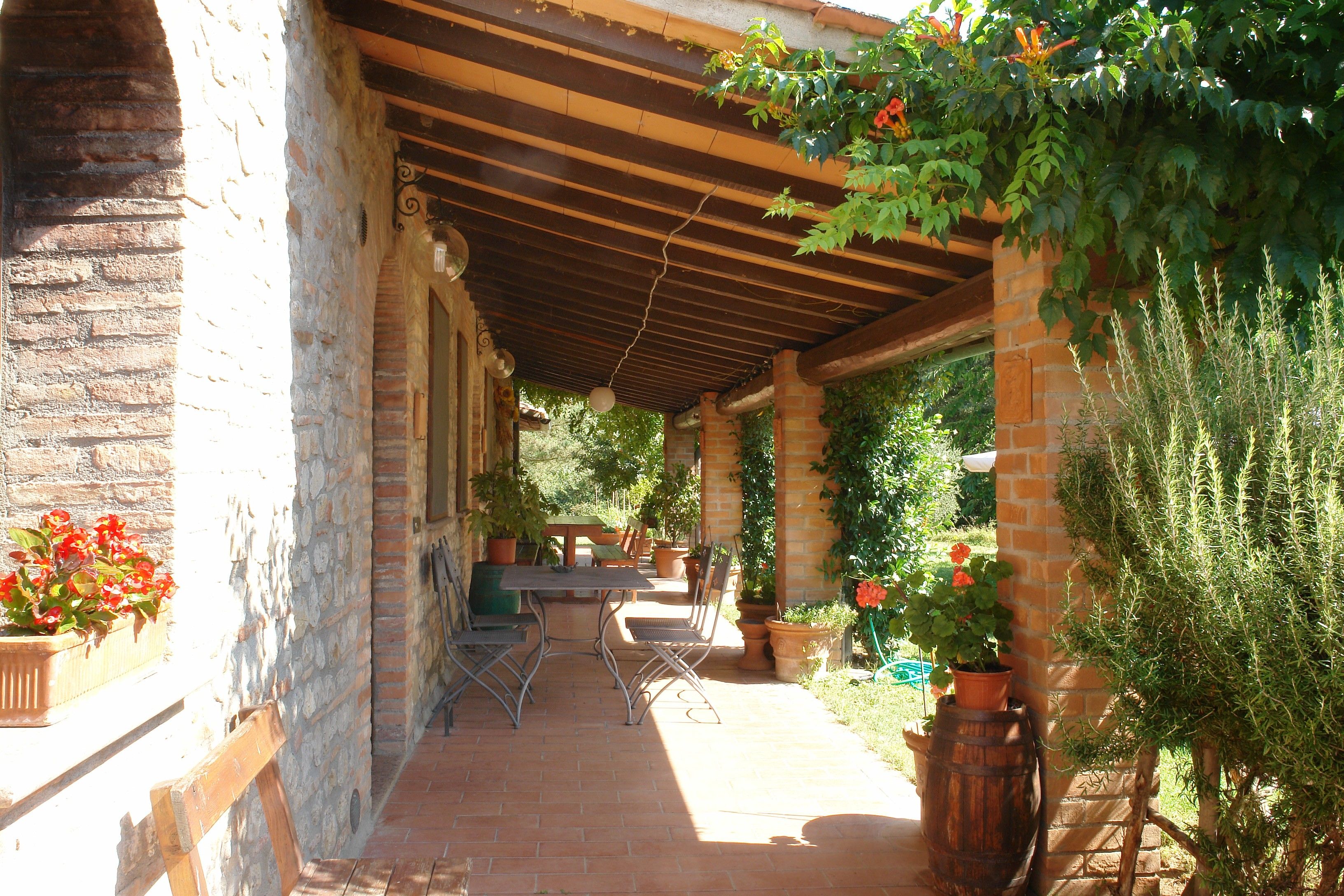 Une terrasse extérieure avec un mur en briques, une pergola en bois et des plantes en pot.