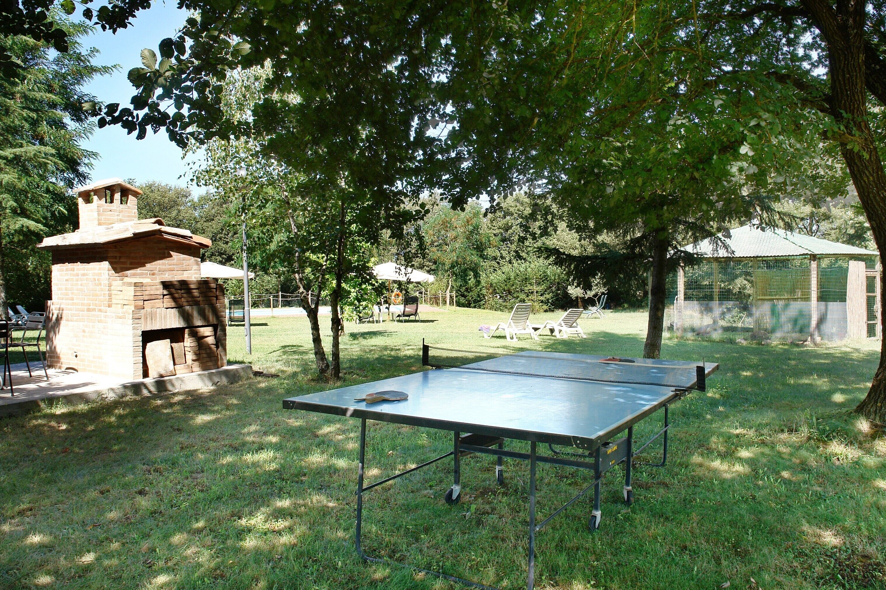 Una xemeneia de totxins a l'aire lliure, una taula de ping-pong i una zona coberta per seure en un ambient similar a un parc.