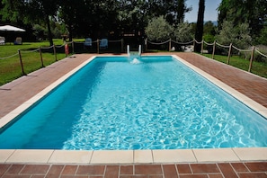 Una piscina rectangular con superficie de agua azul cristalina, rodeada por un borde de ladrillo y una valla de malla.
