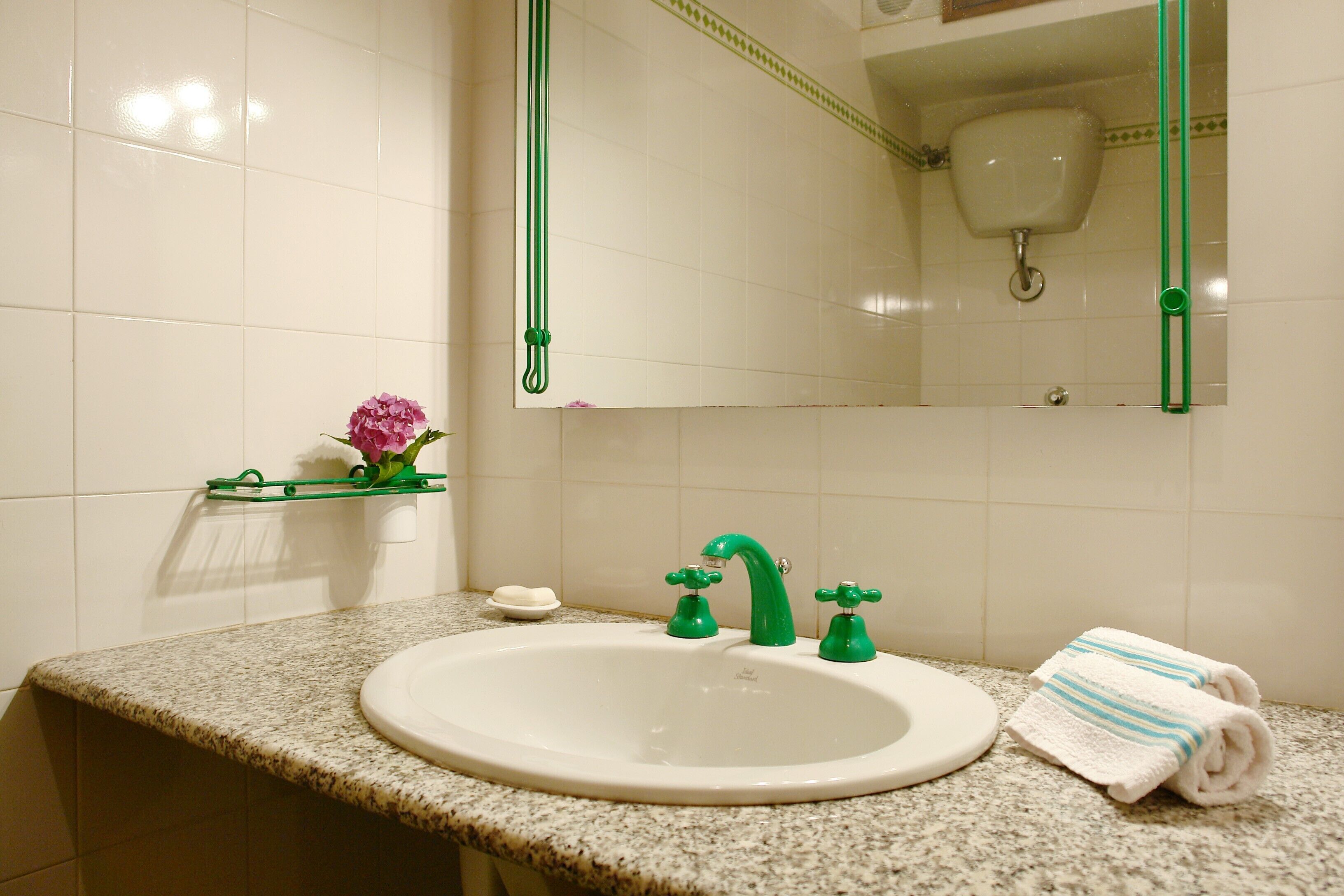 Un baño con un lavamanos blanco, grifos verdes, un espejo y una toalla sobre la encimera.