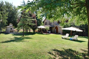 Ein Garten mit einem Steinhaus, zwei weißen Stühlen unter einem Sonnenschirm und einem kleinen Backsteinbau.