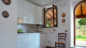Une cuisine avec des meubles blancs, un pot vert, une chaise en bois et une fenêtre donnant sur un paysage verdoyant.