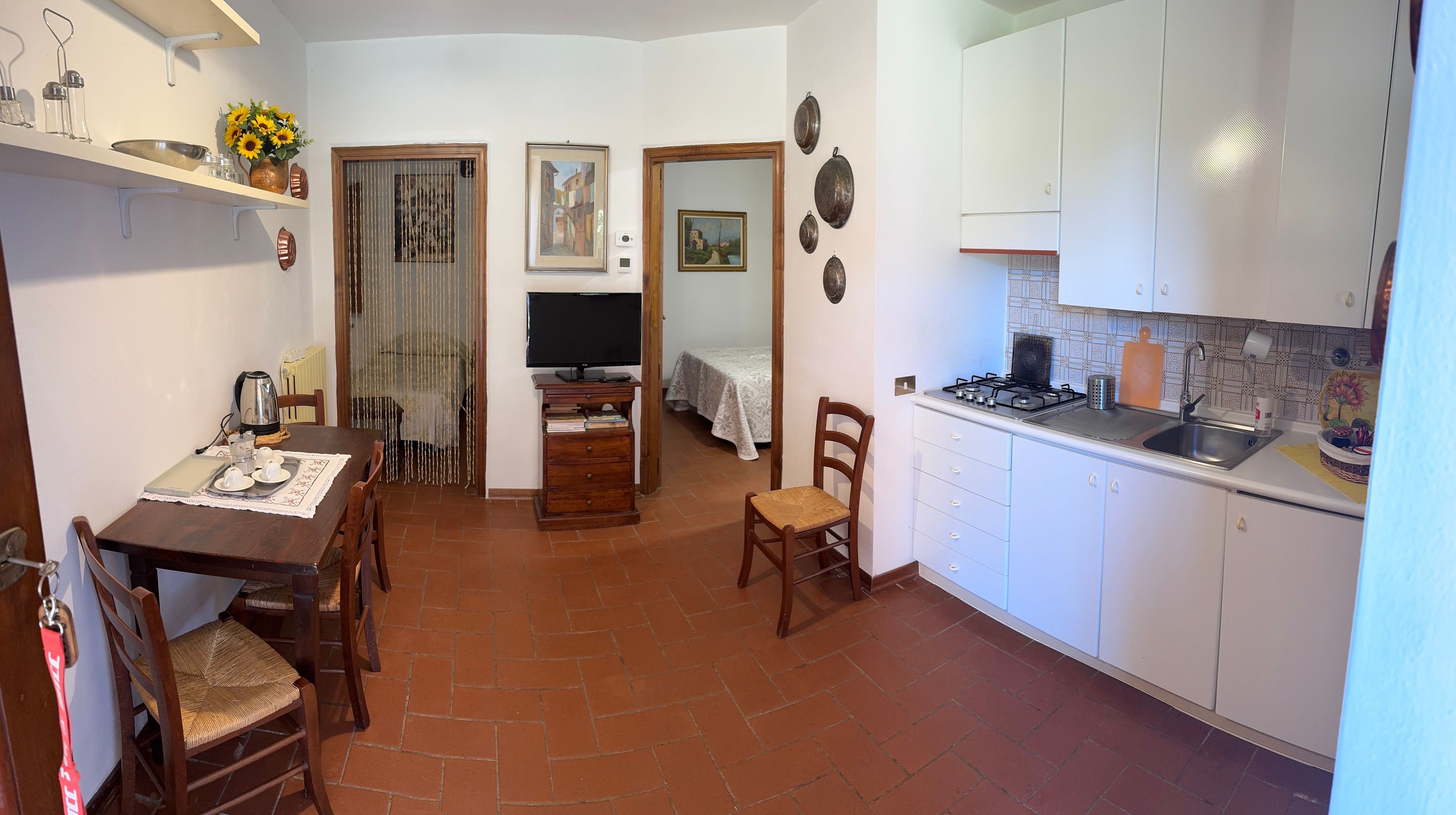 A compact kitchen with a dining area, a TV, and a bed in the adjacent room.