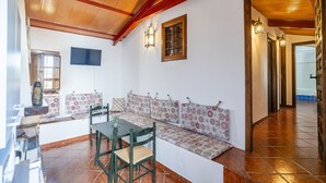 Ein Essbereich mit einem Holztisch und Stühlen, einer Bank mit gemusterten Kissen und einem an der Wand montierten Fernseher.