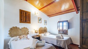 Ein Zimmer mit zwei Betten, Holz-Kopfteilen, einem kleinen Tisch mit Lampe und einem Fenster.