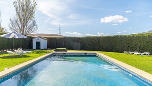 Ein rechteckiger Pool mit Fliesenrand, umgeben von einer Rasenfläche mit Liegestühlen und einer kleinen Gartenhütte.