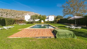 A swimming pool with a tiled deck, surrounded by grass and white lounge chairs. - Cubo's Casa Rural San Cristobal Cortijo el Puntal / rural / communal pool / large outdoor areas / views / free wifi (Teba)