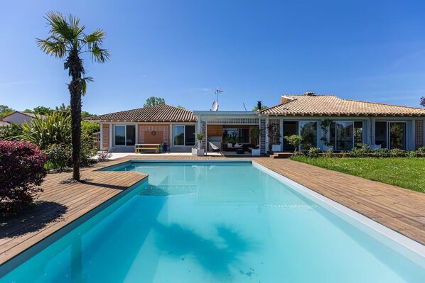 Une maison moderne dotée d’une piscine, de grandes fenêtres et d’un espace patio.