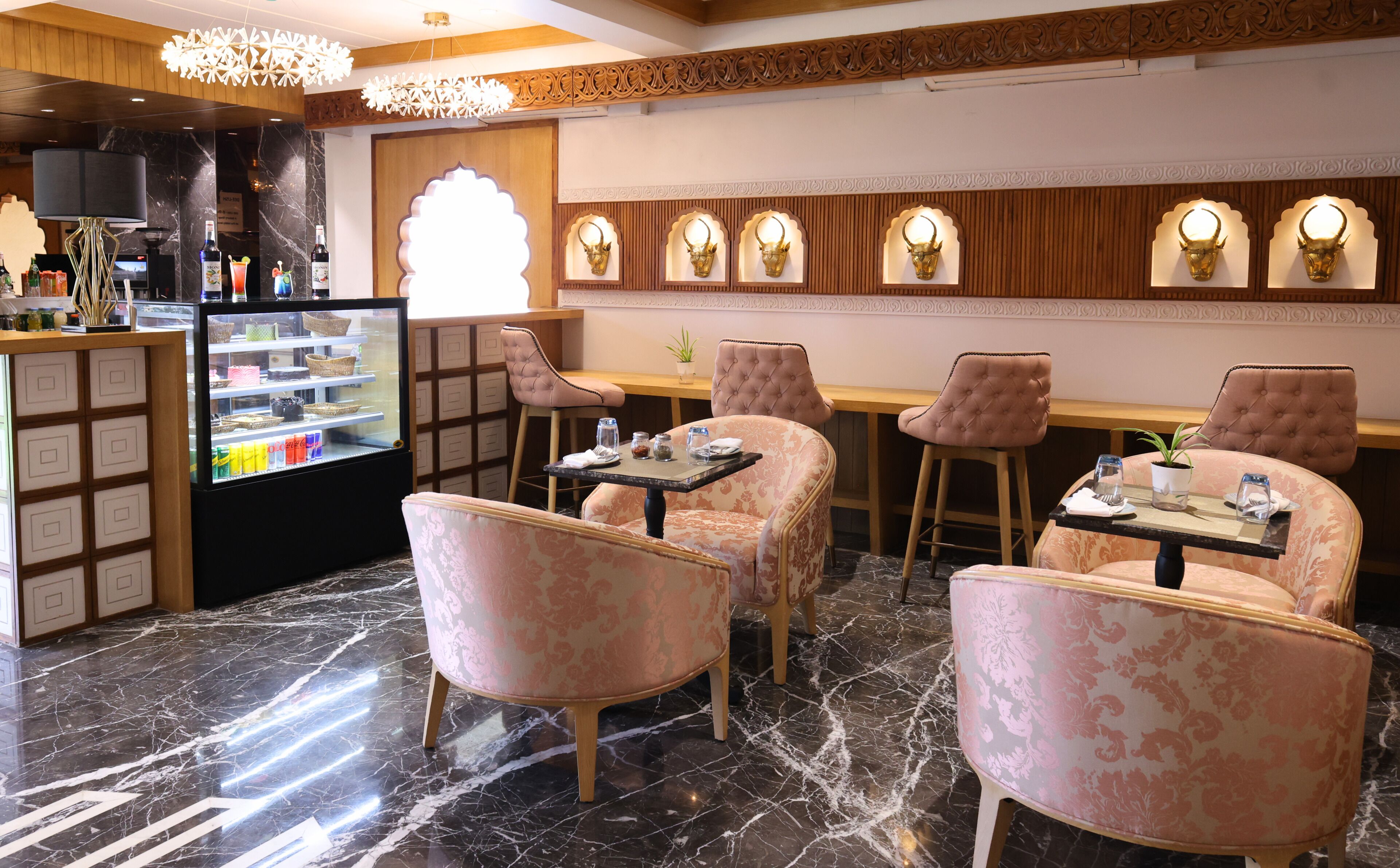 Ein Restaurantinneres mit Marmorböden, gepolsterten Stühlen, einer Dessertauslage und dekorativen Wandleuchten.