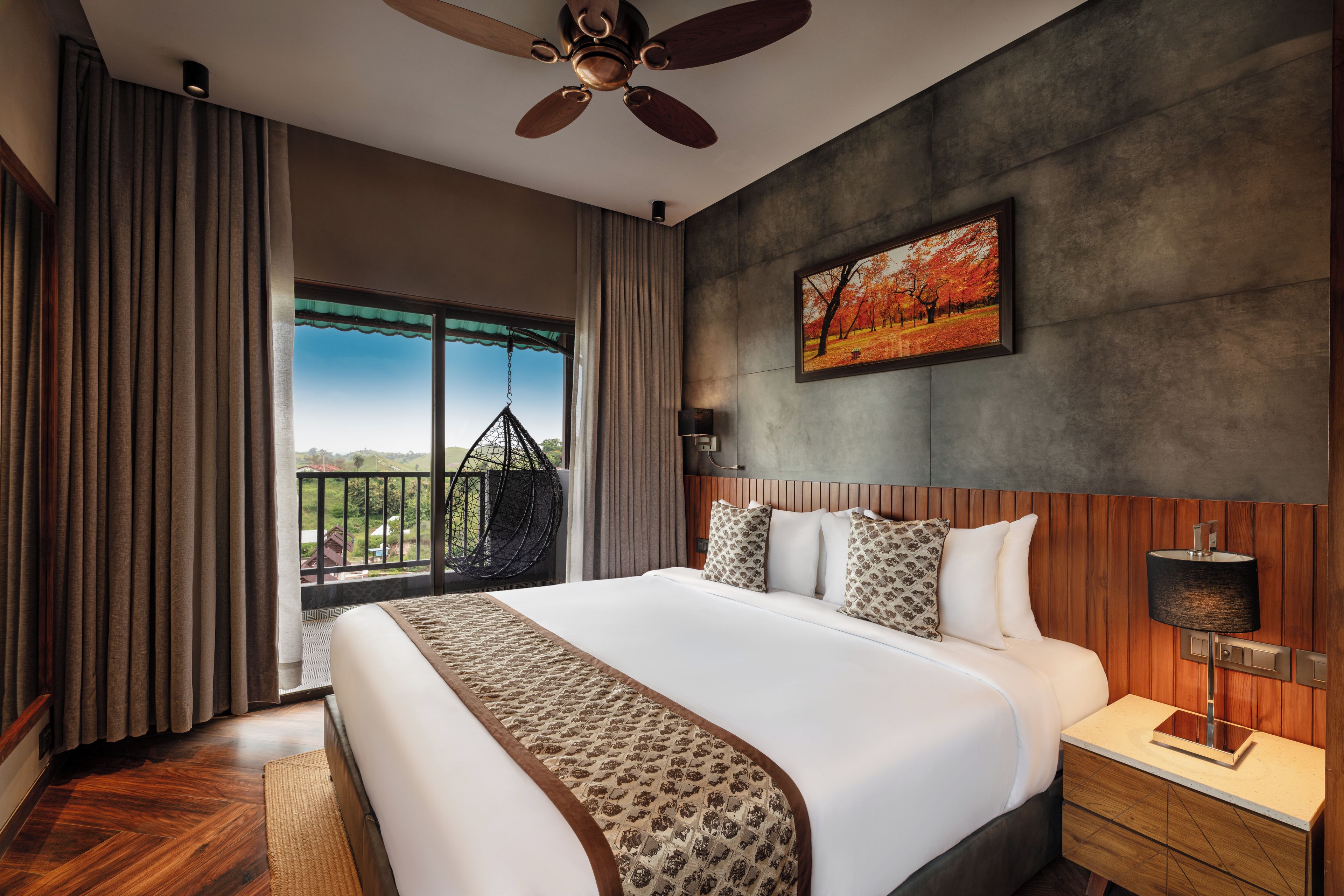 A hotel room with a large bed, a ceiling fan, a view of the outdoors, and a painting on the wall.
