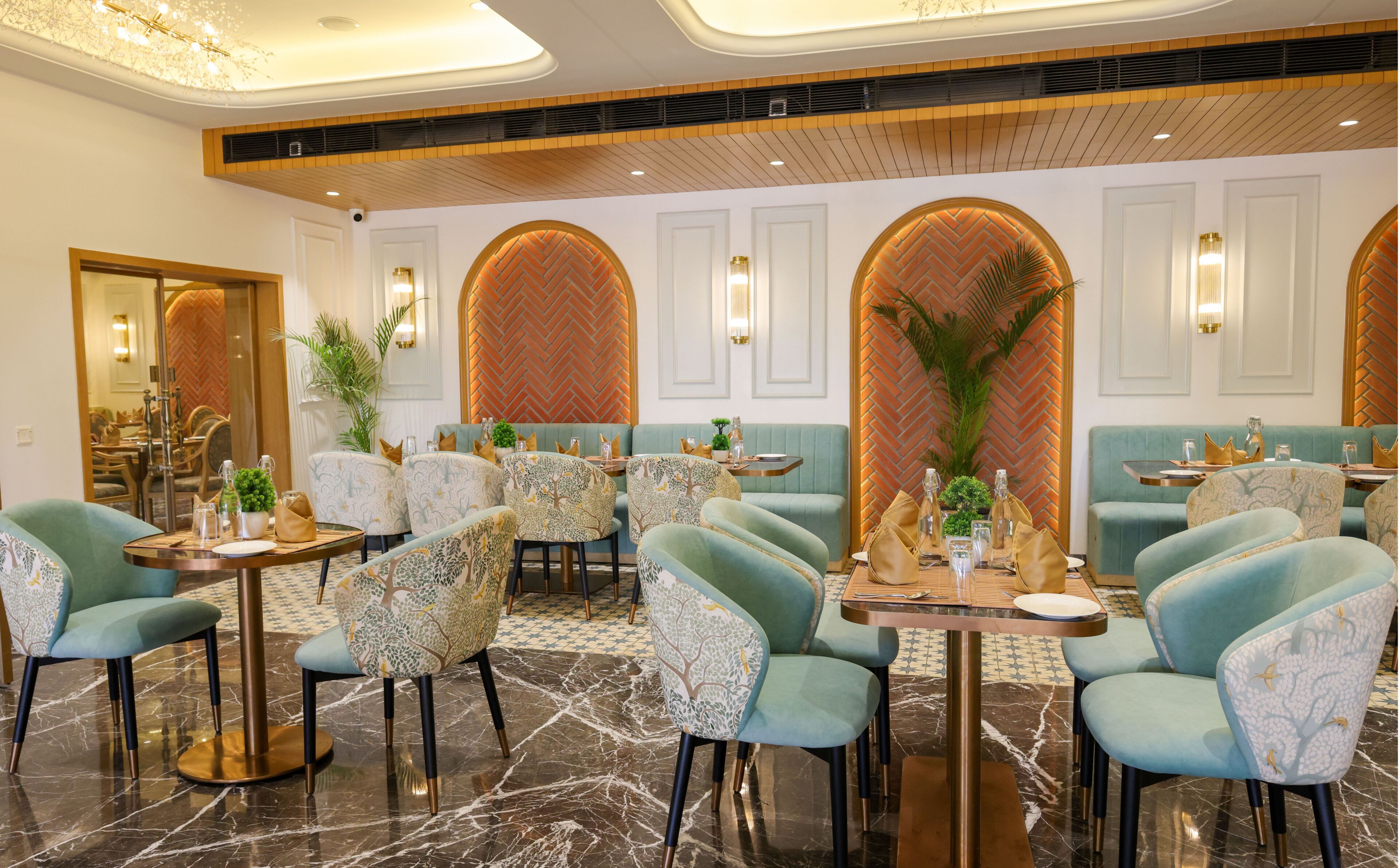 Un restaurante con mesas redondas, sillas color turquesa y una pared con motivo de espiga.