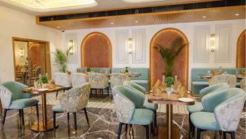 Un restaurante con mesas redondas, sillas color turquesa y una pared con motivo de espiga.