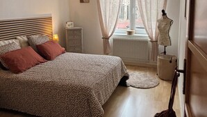 Un dormitorio con cama, cómoda, un maniquí y una ventana con cortinas.