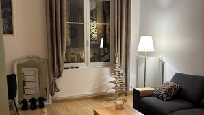 Una sala de estar con una mesa de centro de madera, un sofá negro, una lámpara y una ventana con cortinas.