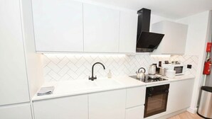 Una cocina moderna con armarios blancos, un lavamanos de acero inoxidable, horno empotrado y microondas.