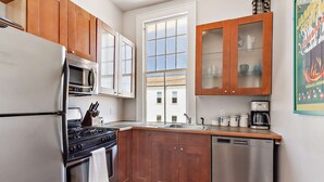 A kitchen with wooden cabinets, a stainless steel refrigerator, a stove, and a dishwasher. - Stylish Freret Street Loft w/Balcony & Parking! (New Orleans)