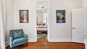 A hallway with a bed, a blue armchair, and two framed posters on the walls. - Stylish Freret Street Loft w/Balcony & Parking! (New Orleans)