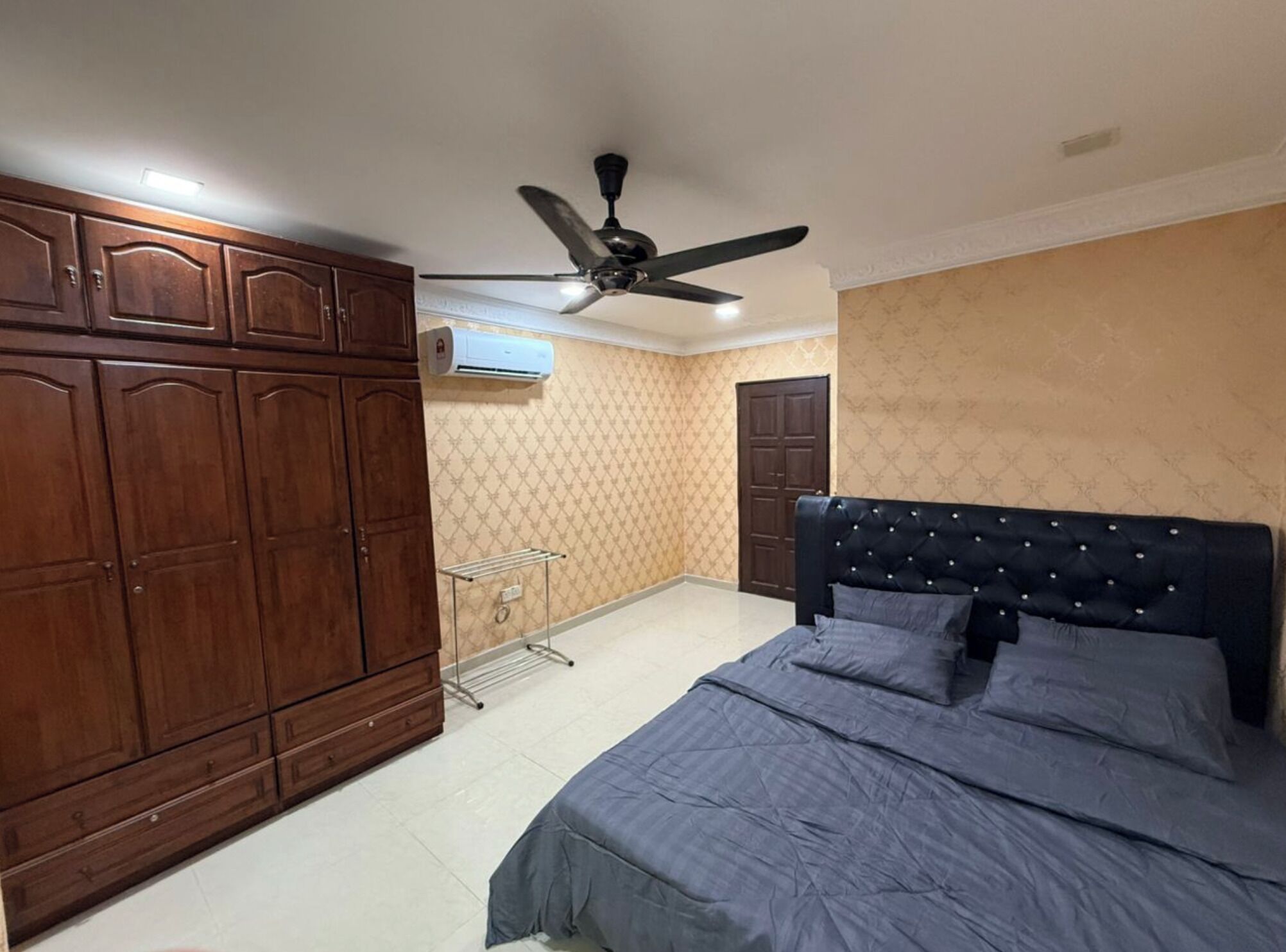 A bedroom with a bed, wardrobe, ceiling fan, and an air conditioning unit.