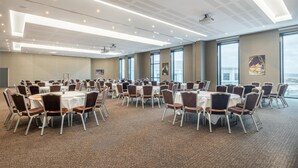 A large conference room with multiple round tables and chairs, large windows, and a high ceiling with recessed lighting. - CDG Airport Terminal Hotel, Paris (Tremblay-en-France)