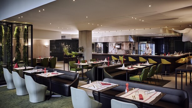 A modern restaurant with black and green seating, a central bar, and a visible kitchen area. - CDG Airport Terminal Hotel, Paris (Tremblay-en-France)