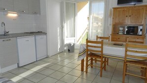 A compact kitchen with white cabinets, a microwave, and a dining area with wooden chairs and a table. - 3-room apartment, 5 beds with private garage in Bormes-les-Mimosas (Bormes-les-Mimosas)