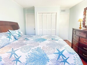 A bedroom with a bed, a dresser, and a door with shutters. - Tilghman Beach and Racquet Club 170 (North Myrtle Beach)