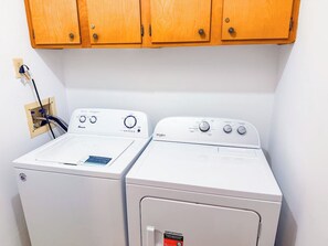 Deux machines à laver à chargement frontal se trouvent dans une buanderie, au-dessus desquelles sont installés des meubles de rangement en bois.