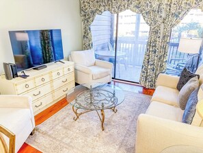 A living room with a sofa, a glass coffee table, a TV, and a dresser. - Tilghman Beach and Racquet Club 170 (North Myrtle Beach)