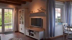 Una habitación con televisor sobre un mueble de madera, una mesa de comedor con sillas y un ventanal corredero al exterior.