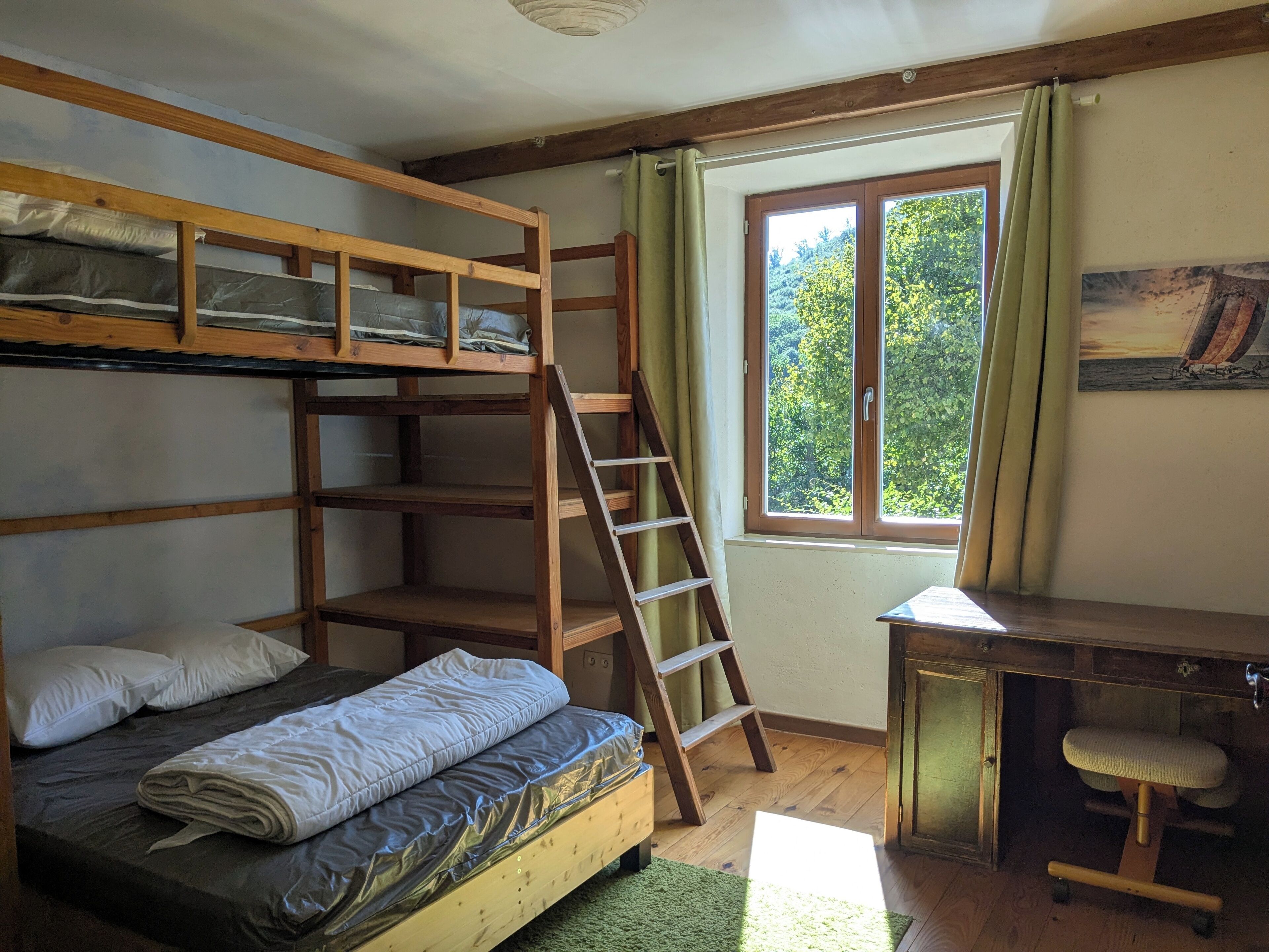 A bunk bed with a desk and chair, a ladder, and a window with curtains.