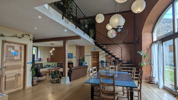 Un vaste espace de vie agrémenté d’un escalier en bois, d’une table à manger avec des chaises et d’une cheminée.