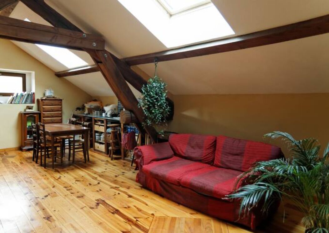 A loft-style room with a wooden floor, a red sofa, a dining table with chairs, and a bookshelf.