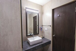 A bathroom with a white sink, a mirror, a dark door, and a light switch on the wall. - SKYLAR Tirupati (Tirupati)