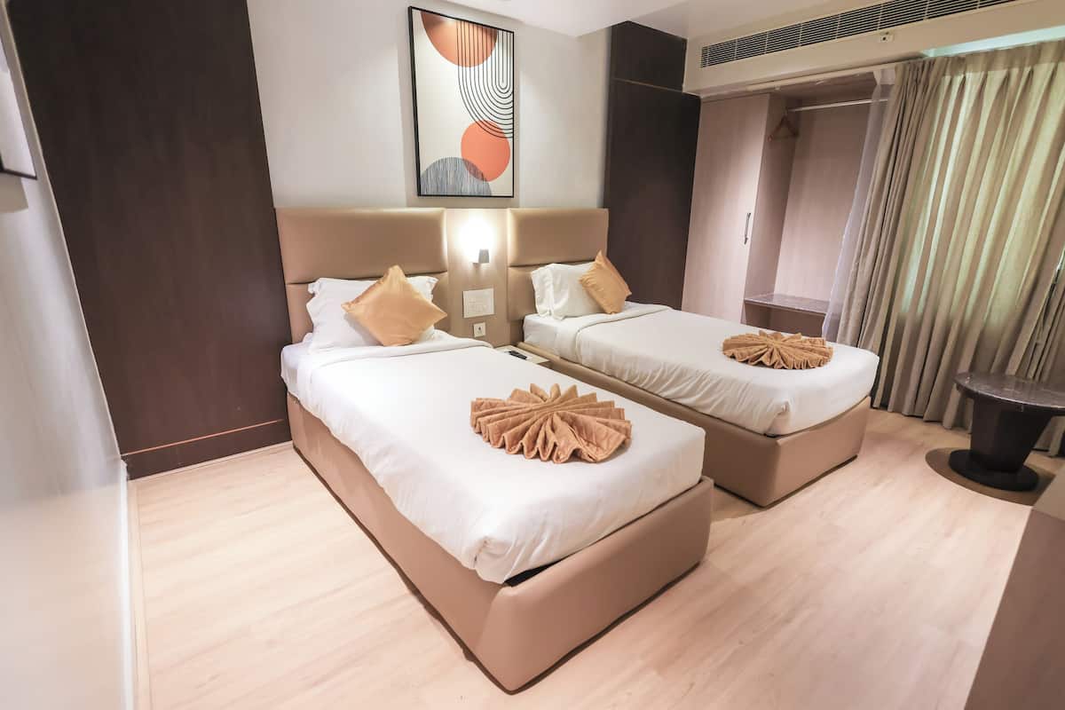 A hotel room with two beds, a headboard, a wall-mounted artwork, a bedside table, and a curtain.