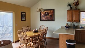 Een eetruimte met een houten tafel en stoelen, een kroonluchter en een keuken met houten kastjes en een prullenbak.