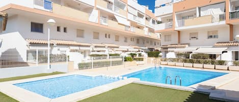 Un edificio residencial con piscina, varios balcones y un césped bien cuidado.