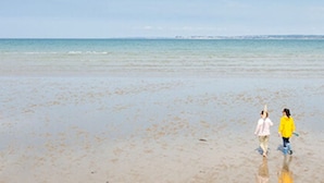 Una playa con dos personas caminando.