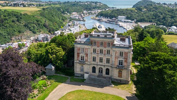 Un grande edificio storico con facciata simmetrica, un ingresso centrale e un prato verde circostante.