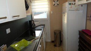 Eine kompakte Küche mit weißen Schränken, einer Edelstahl-Spüle, einer Kaffeemaschine, einem Mülleimer und einem Kühlschrank.