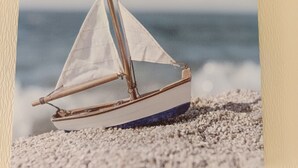 Ein kleines Segelboot an einem Kiesstrand.