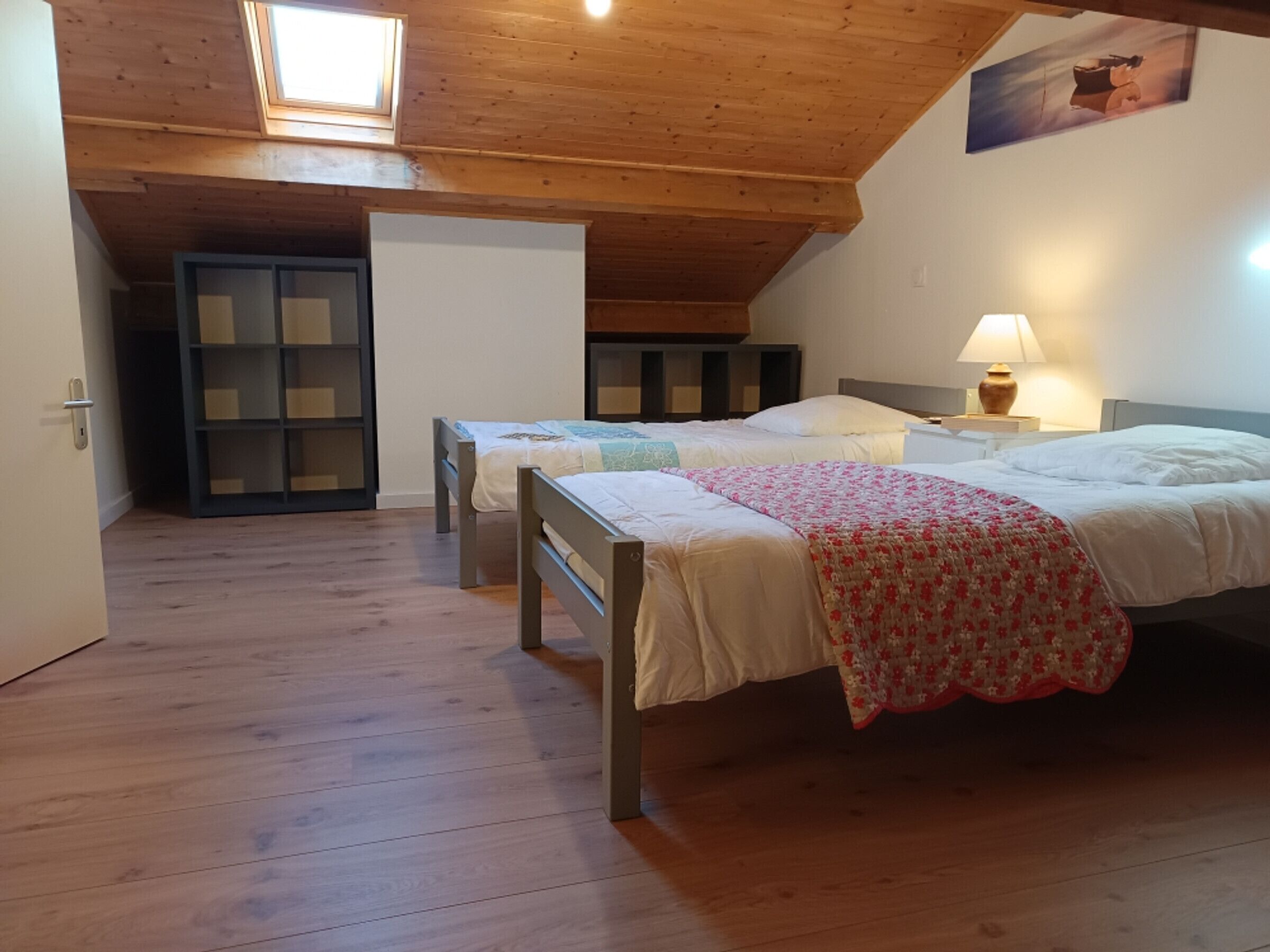 Ein Zimmer mit zwei Betten, Holzböden, einem Oberlicht und einem Bild an der Wand.