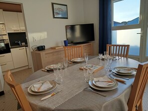 En matplats med ett bord dukat för fyra personer, en tv på ett skåp och ett fönster med utsikt.