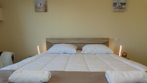 Ein ordentlich bezogenes Bett mit weißen Leinen und zwei Kissen, ein hölzernes Kopfende sowie zwei an der Wand hängende Bilder.