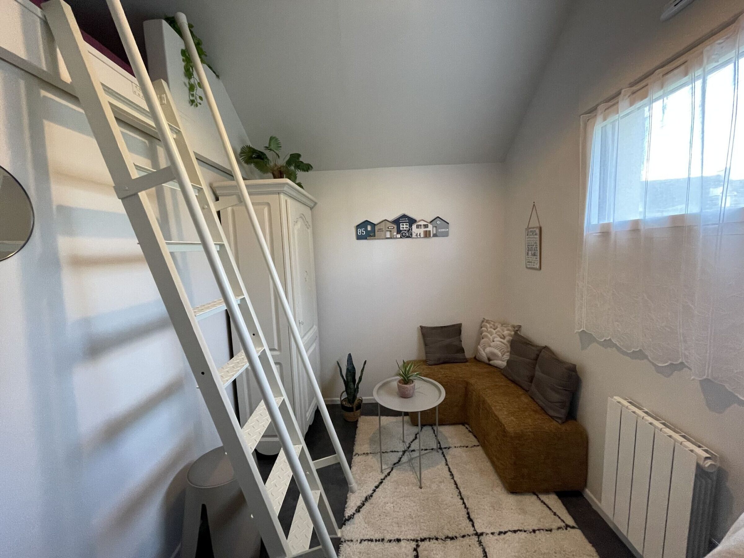 Un espacio habitable compacto con una escalera blanca, una pequeña mesa redonda, un sofá marrón y un radiador.