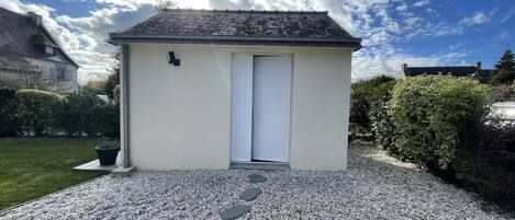 A small, single-story building with a white exterior and a dark roof, featuring a white door and a small black mailbox on the wall.