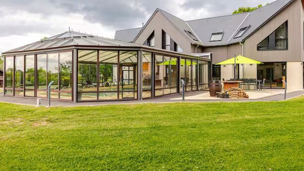 A modern house with a glass conservatory, a patio area, and a large lawn.