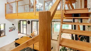 A modern interior with a wooden staircase, glass railings, and a dining area with a wooden table.