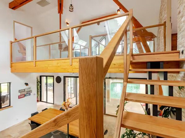 A modern interior with a wooden staircase, glass railings, and a dining area with a wooden table. - Architect house with heated pool and secure park (Soulitré)