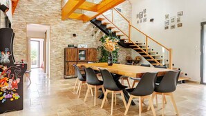 A spacious dining area with a wooden table and chairs, a staircase, and a kitchen in the background.