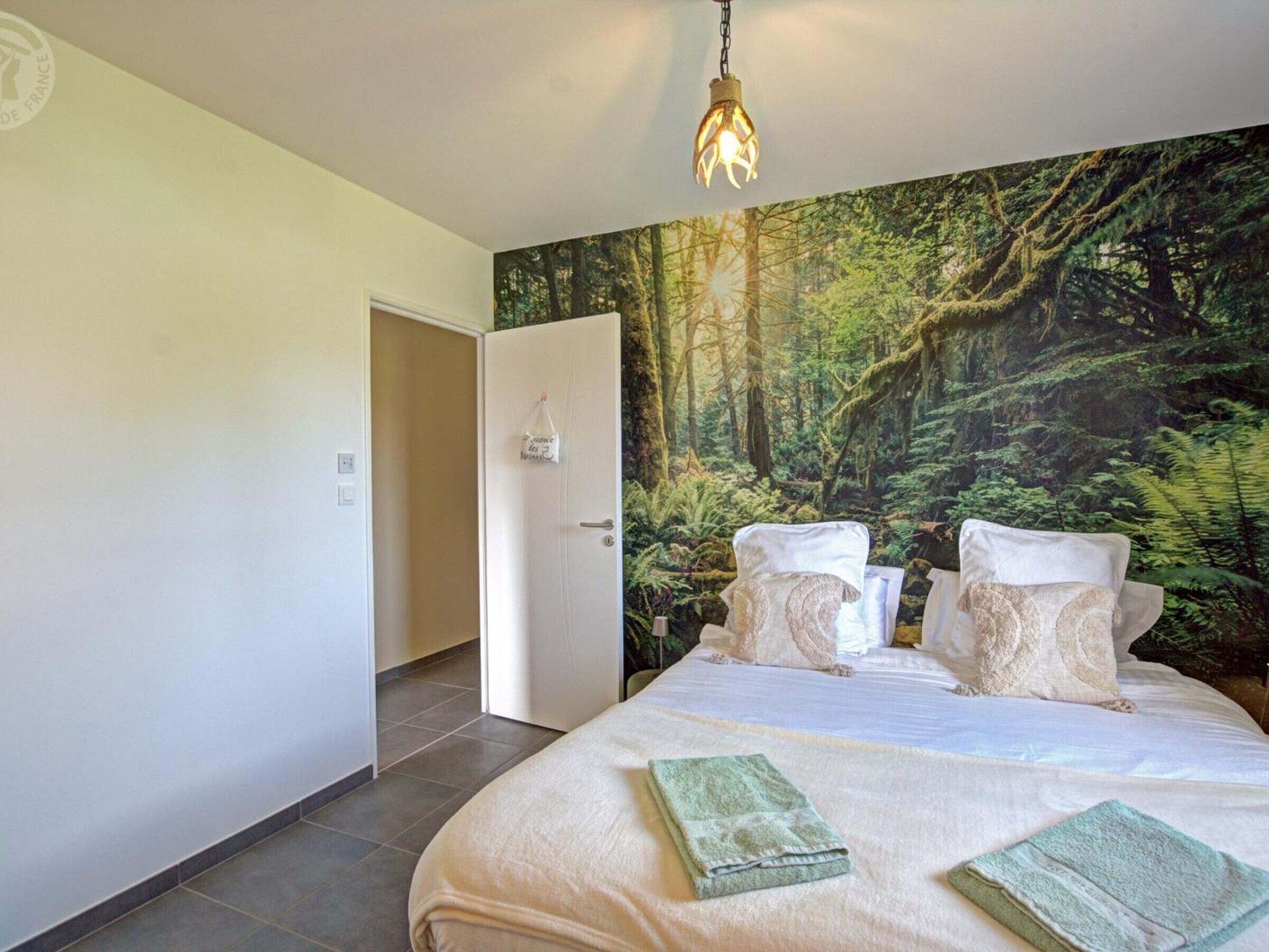 Un dormitorio con una cama grande, un mural temático de bosque y una lámpara colgante.